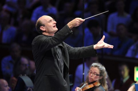 Andrew Manze wearing black clothes with both arms lifted and holding a white baton
