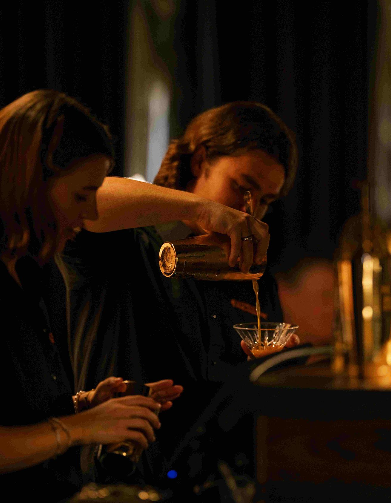 Two people pouring drinks behind a bar