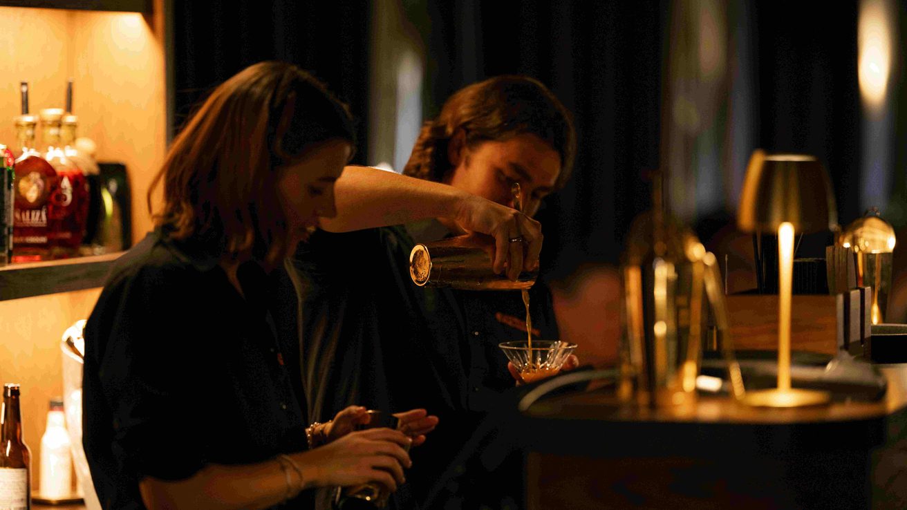 Two people pouring drinks behind a bar