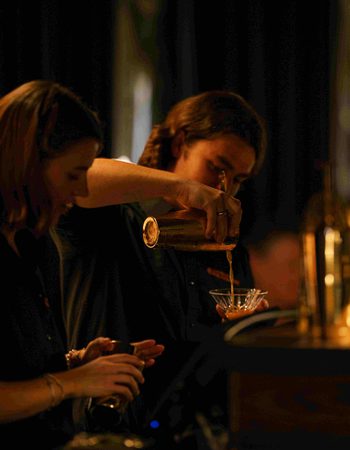 Two people pouring drinks behind a bar