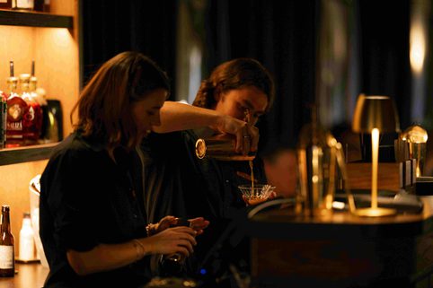 Two people pouring drinks behind a bar