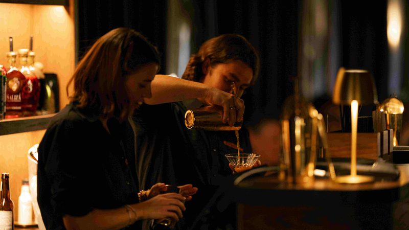 Two people pouring drinks behind a bar