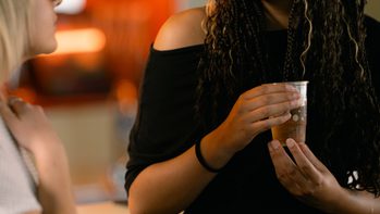 Young black woman wearing glasses talking to somebody near the bar.