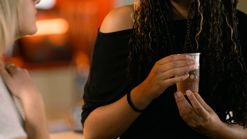 Young black woman wearing glasses talking to somebody near the bar.