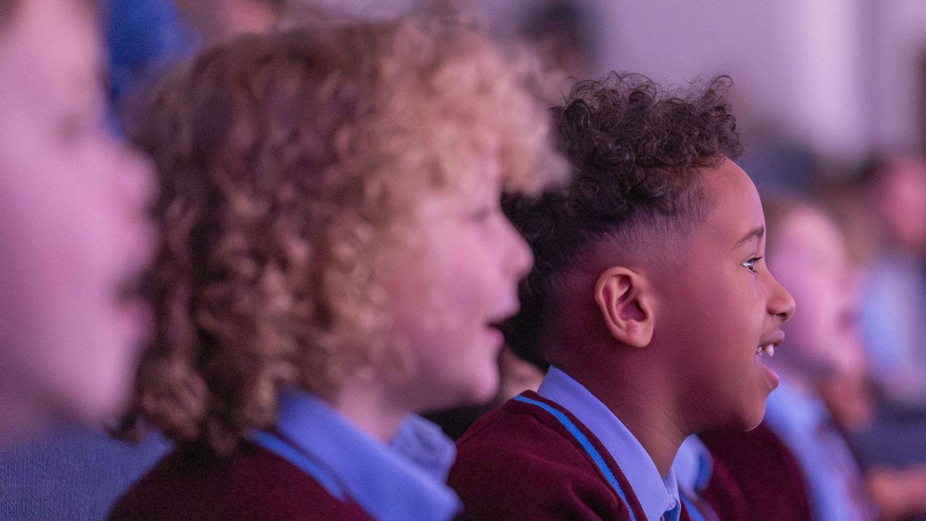 Children in school uniform smiling and staring at the stage