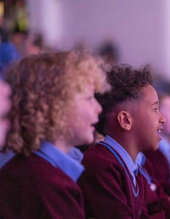 Children in school uniform smiling and staring at the stage