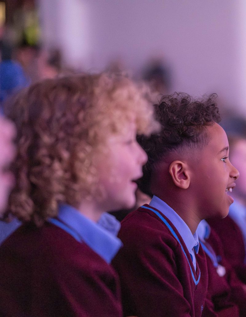Children in school uniform smiling and staring at the stage