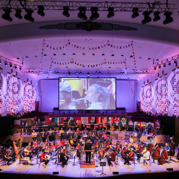 Liverpool Philharmonic Hall stage full of musicians, decorated with colourful flags, bunting and light projections on the walls