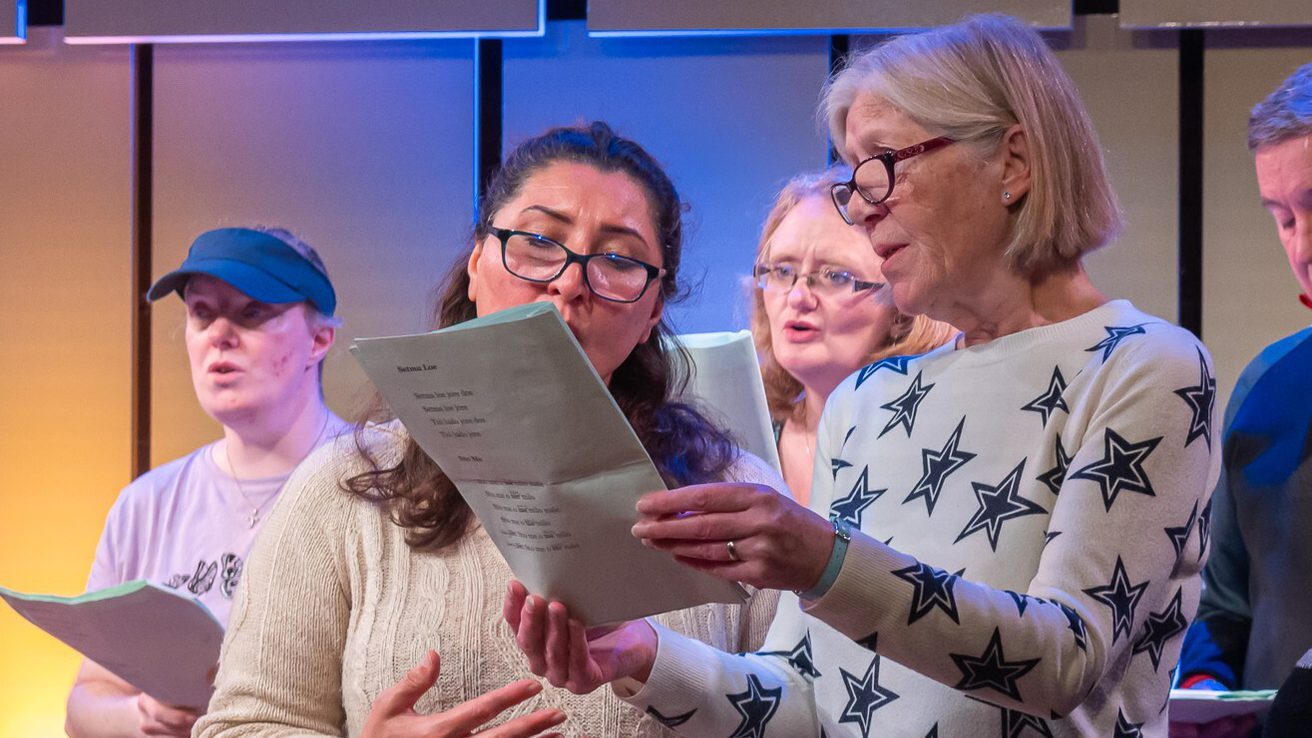 Two women standing up and singing from a sheet of paper
