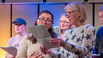 Two women standing up and singing from a sheet of paper