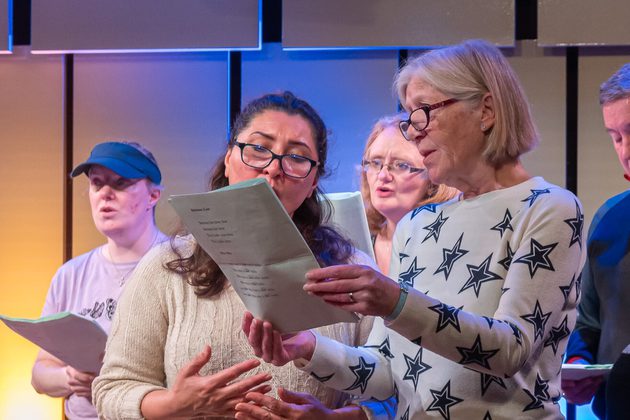 Two women standing up and singing from a sheet of paper
