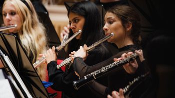 Three girls dressed in black playing the violin on stage