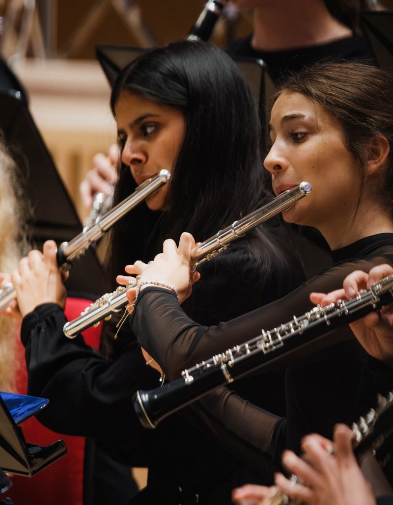 Three girls dressed in black playing the violin on stage