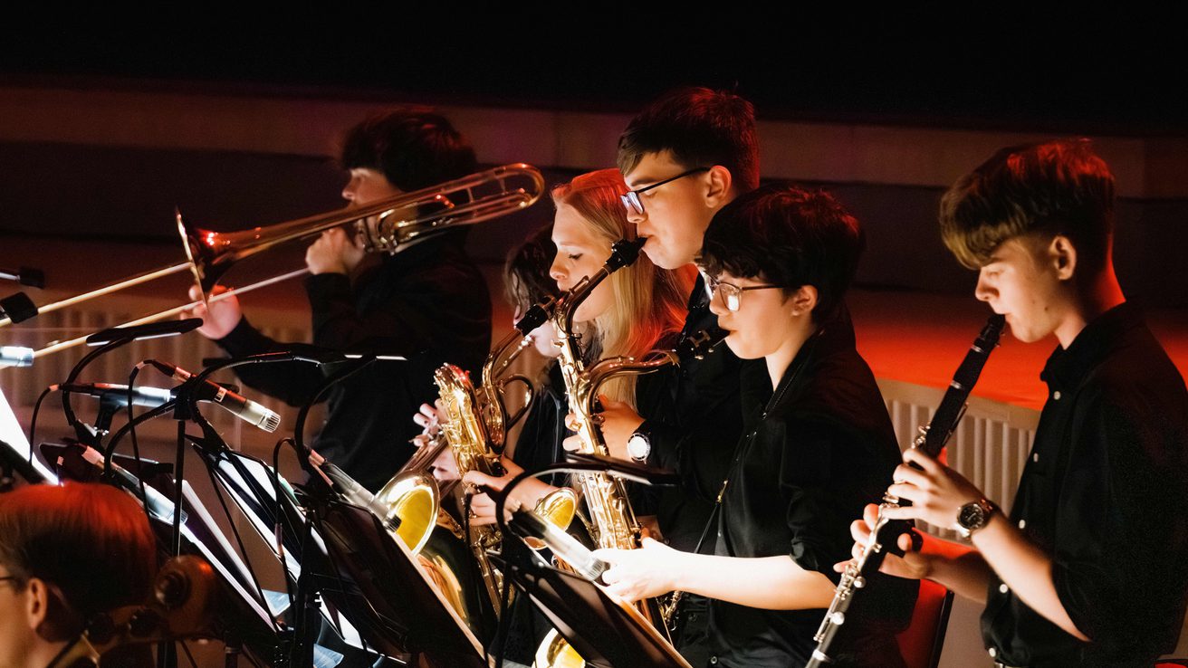 A row of young musicians performing brass and woodwind instruments on stage