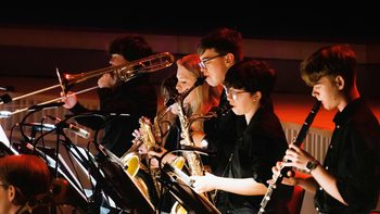 A row of young musicians performing brass and woodwind instruments on stage