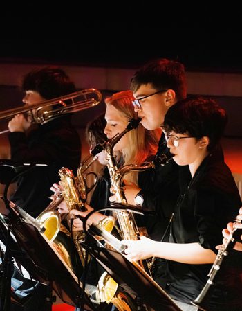 A row of young musicians performing brass and woodwind instruments on stage