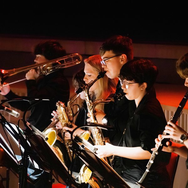A row of young musicians performing brass and woodwind instruments on stage