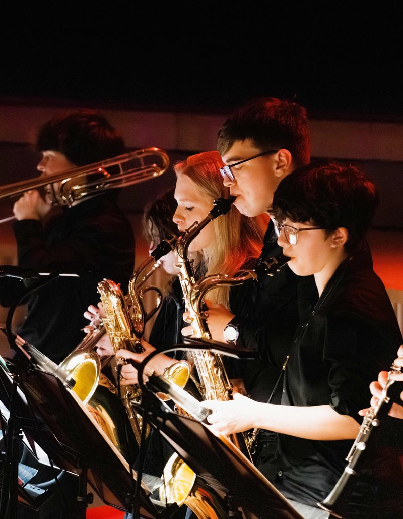 A row of young musicians performing brass and woodwind instruments on stage