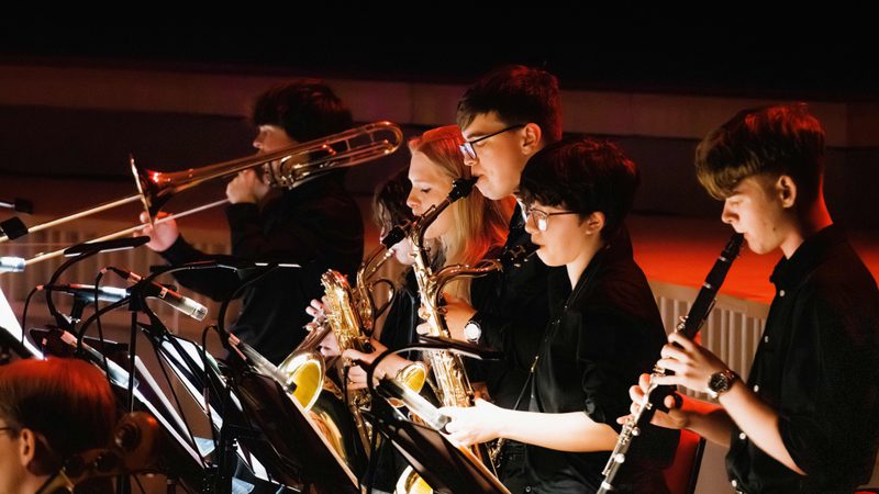 A row of young musicians performing brass and woodwind instruments on stage