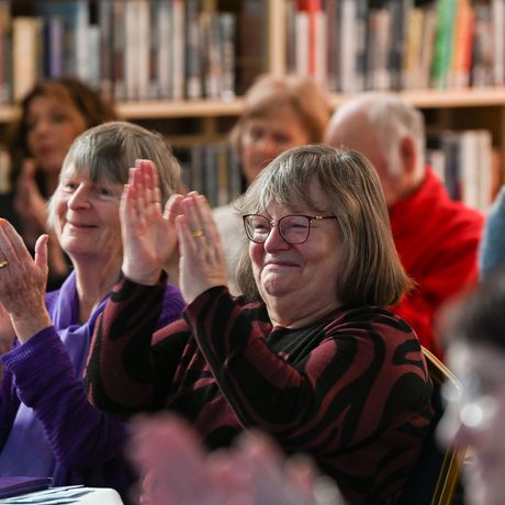 A close up of two women with short grey hair smiling and clapping in an audience