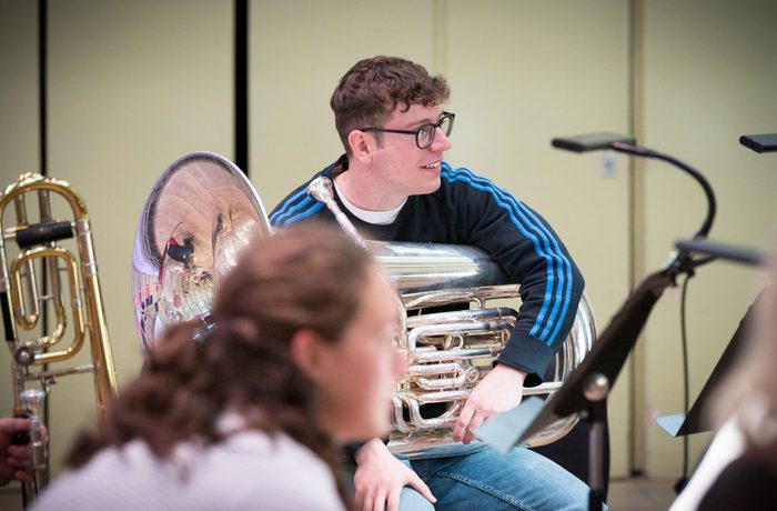 Emerging Musician and tuba player Ramon Branch Biescas in rehearsal holding his instrument, smiling and wearing a blue jumper