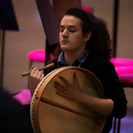 Emerging Musician and percussion player Stan Talman in rehearsal wearing a blue shirt and jumper and playing a drum