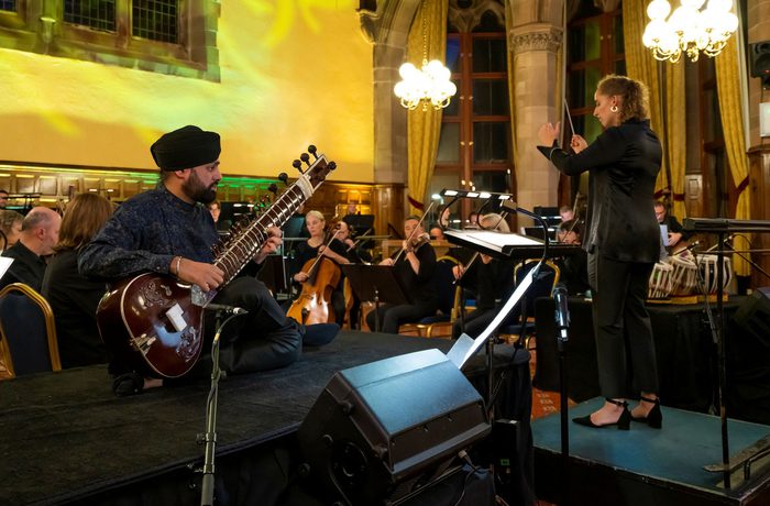 Sitar player Jasdeep Singh Degun sits playing in front of the Royal Liverpool Philharmonic Orchestra