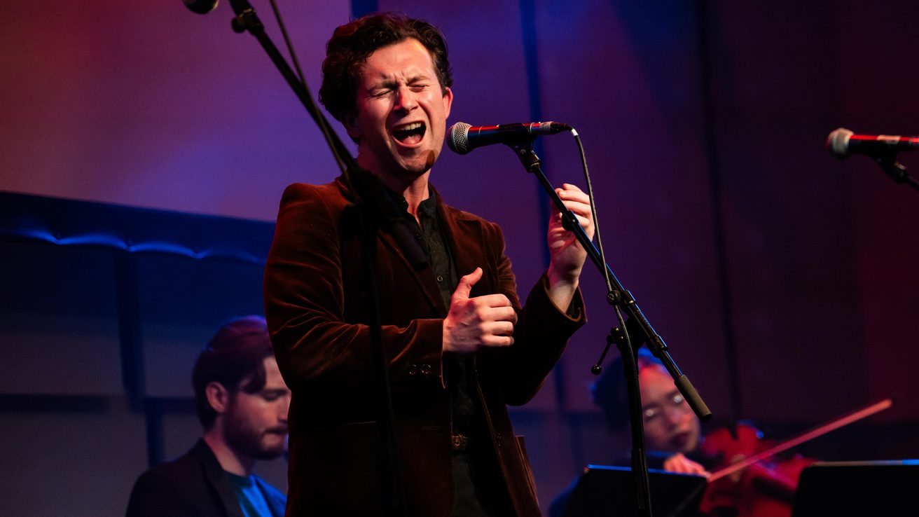 MT Jones in a velvet jacket singing on stage in the Music Room