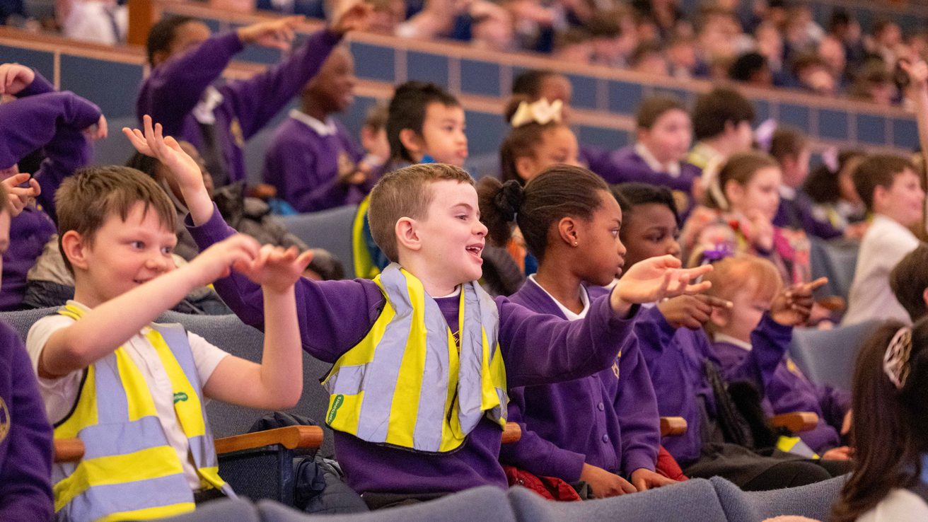 A group of schoolchildren in purple uniforms and high-vis jackets clapping and laughing in Liverpool Philharmonic Hall