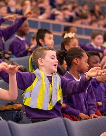 A group of schoolchildren in purple uniforms and high-vis jackets clapping and laughing in Liverpool Philharmonic Hall