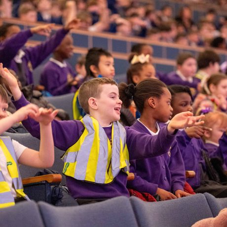 A group of schoolchildren in purple uniforms and high-vis jackets clapping and laughing in Liverpool Philharmonic Hall