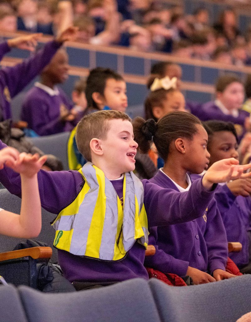 A group of schoolchildren in purple uniforms and high-vis jackets clapping and laughing in Liverpool Philharmonic Hall