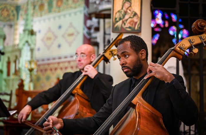Two double bass players from the Royal Liverpool Philharmonic Orchestra wearing all black and performing in a church