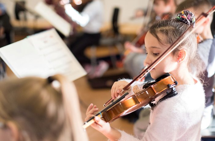 A young girl with dark hair in a pink fluffy jumper playing the violin
