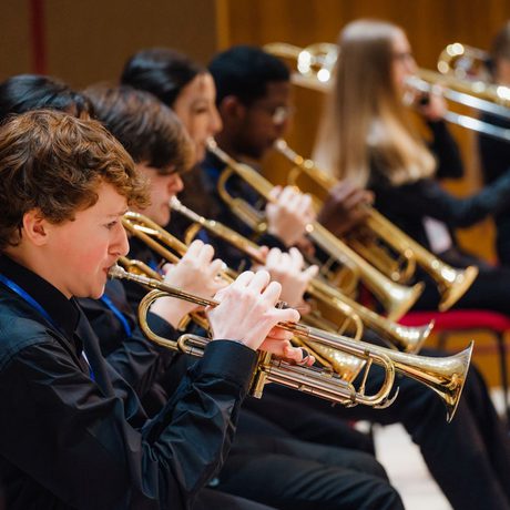 A row of musicians from Liverpool Philharmonic Youth Orchestra all wearing black and playing trumpets and trombones