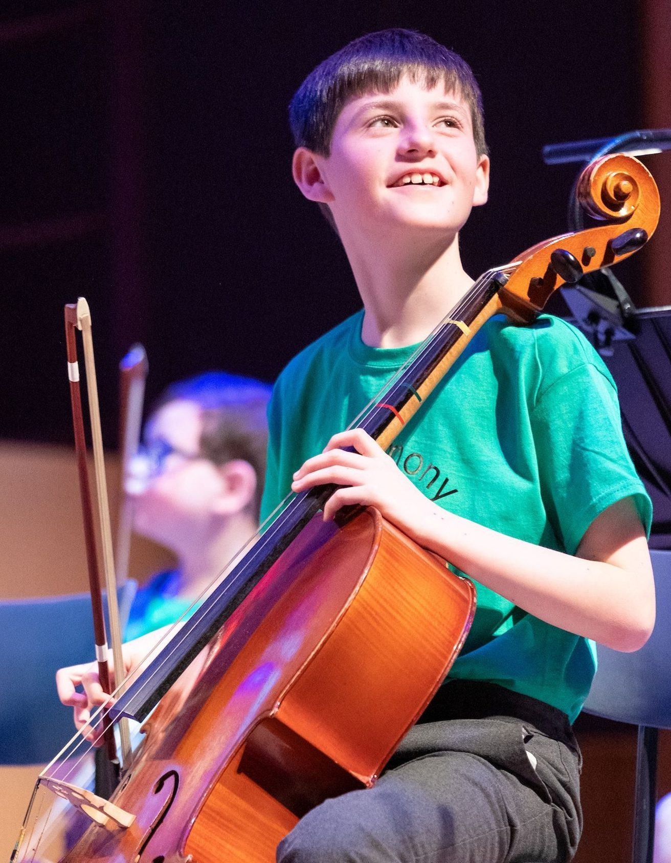 Smiling boy playing the cello looking out from the stage to the audience
