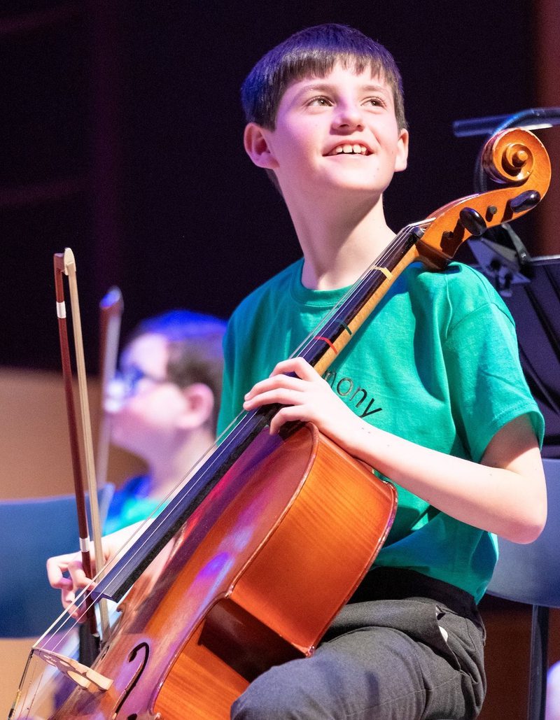 Smiling boy playing the cello looking out from the stage to the audience