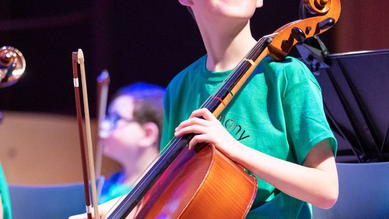 Smiling boy playing the cello looking out from the stage to the audience