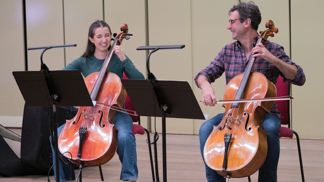 Two musicians laughing and playing the cello