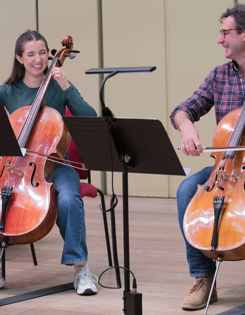 Two musicians laughing and playing the cello