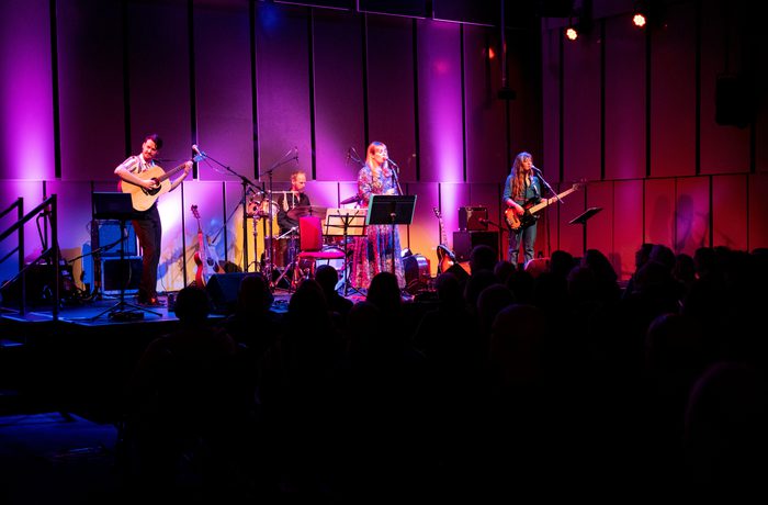 Musicians on stage in the Music Room with a crowd in the foreground