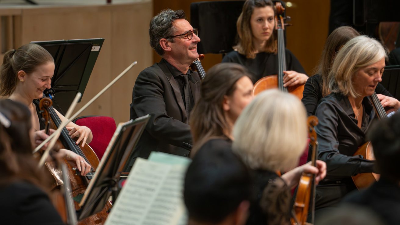 Cello section of the orchestra wearing all black and smiling playing their instruments