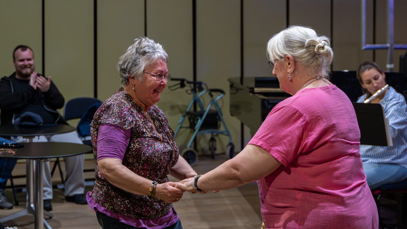 two older audience members facing each other, holding hands and dancing together