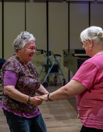 two older audience members facing each other, holding hands and dancing together