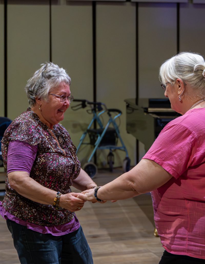two older audience members facing each other, holding hands and dancing together