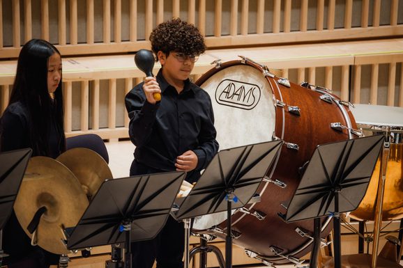 Young boy wearing black looking at a black music stand and playing with a black maraca