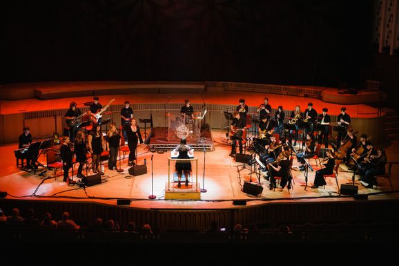 all members of the youth session band performing on stage with orange hue lighting