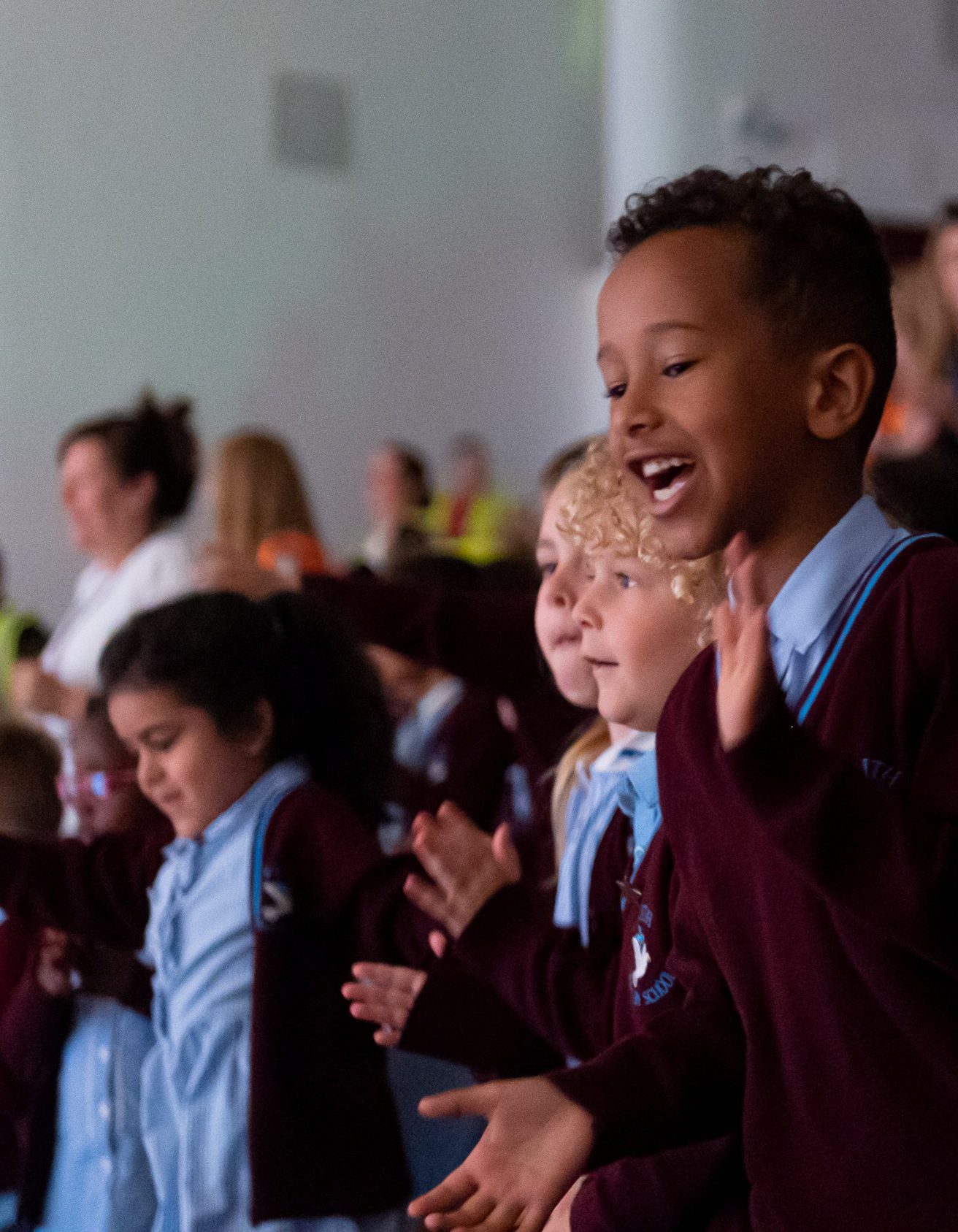 Young audience members wearing blue and burgundy school uniform smiling and clapping