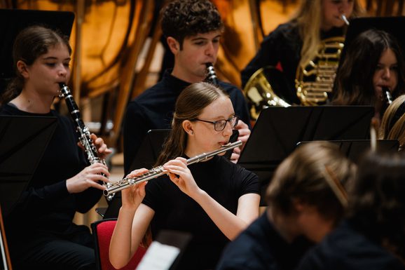 Young girl wearing black clothes and black glasses playing the flute