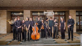 Members of the Youth Company standing in a row outside Liverpool Philharmonic Hall wearing black and holding their instruments